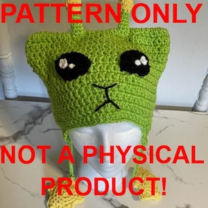 May include: A lime green crocheted hat with large black eyes, white highlights, and a stitched black mouth. The hat has two yellow antennae and ear flaps. The text "PATTERN ONLY" and "NOT A PHYSICAL PRODUCT!" are in red.
