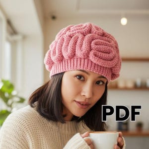 Könnte beinhalten: Eine rosa Strickmütze mit einem gehirnartigen Design. Die Mütze hat eine hellrosa Farbe und ein strukturiertes, dreidimensionales Aussehen. Das Wort "PDF" befindet sich in der unteren rechten Ecke des Bildes.