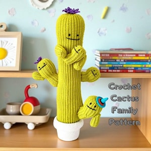 May include: A handmade, crochet cactus family in a white pot. The main cactus is tall and green with a purple flower on top. Smaller cacti with smiling faces are attached. The text "Crochet Cactus Family Pattern" is visible.