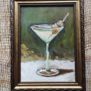 K&ouml;nnte beinhalten: Ein Gem&auml;lde eines Martini-Glases mit Oliven vor gr&uuml;nem Hintergrund, in einem goldenen Rahmen.