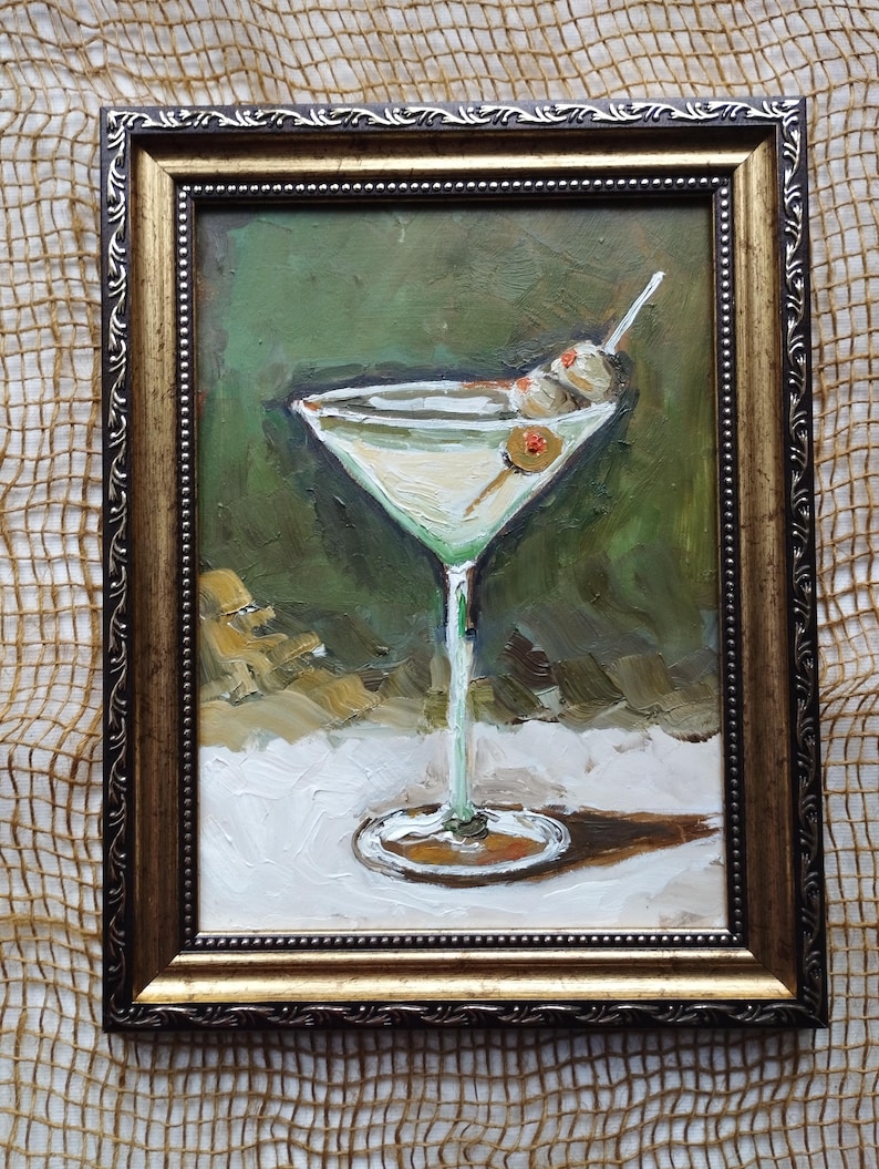 K&ouml;nnte beinhalten: Ein Gem&auml;lde eines Martini-Glases mit Oliven vor gr&uuml;nem Hintergrund, in einem goldenen Rahmen.