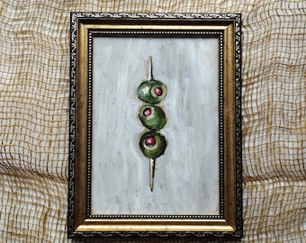 May include: A framed painting of three green olives on a toothpick, painted in a realistic style with visible brushstrokes.
