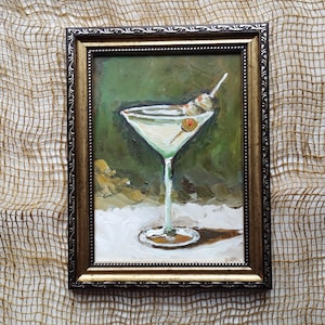 K&ouml;nnte beinhalten: Ein gerahmtes &Ouml;lgem&auml;lde eines Martini-Glases mit zwei gr&uuml;nen Oliven an einem Zahnstocher. Das Glas ist mit einer klaren Fl&uuml;ssigkeit gef&uuml;llt und steht auf einer wei&szlig;en Oberfl&auml;che. Der Hintergrund ist gr&uuml;n und braun.