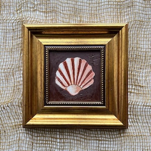 May include: A framed painting of a seashell. The artwork features a fan-shaped shell with alternating stripes of white and reddish-brown against a dark brown background. The painting is encased in a gold-colored frame.
