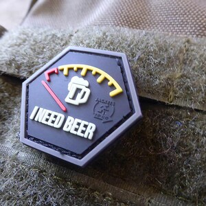 May include: A black and white patch with a fuel gauge design. The gauge is labeled "I need beer" and has a beer mug icon. The gauge is almost empty.