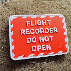 Könnte beinhalten: Ein roter und weißer Patch mit dem Text "FLIGHT RECORDER DO NOT OPEN".