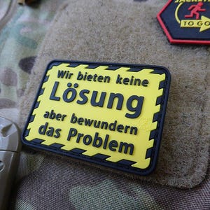 May include: Yellow and black patch with the text "Wir bieten keine Lösung aber bewundern das Problem" in German.