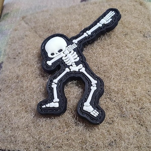 Könnte beinhalten: Ein schwarzer und weißer Skelett-Patch in einer Dabbing-Pose. Der Patch ist aus Stoff und hat einen weißen Umriss.