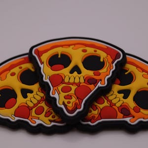 May include: Three pizza slice-shaped patches with a skull design. The patches feature a yellow base with red pepperoni and orange crusts. The skull's eyes and mouth are black, and the patches have a black border.