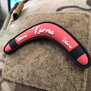 May include: A pink boomerang patch with black trim and white text that reads "Karma Returns".