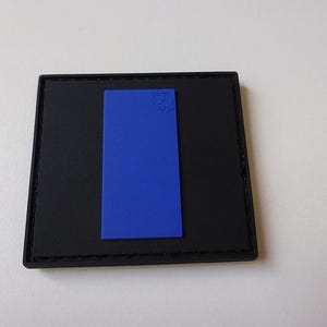 Può includere: Una toppa nera con un rettangolo blu al centro. Il rettangolo contiene il testo "Military" e un simbolo all'interno.