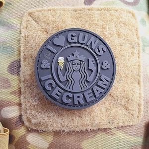 Op de afbeelding: Zwart-witte patch met de tekst "I & GUNS & ICE CREAM" in een cirkel. In het midden van de cirkel staat een gestileerde afbeelding van een zeemeermin die een ijshoorn vasthoudt.