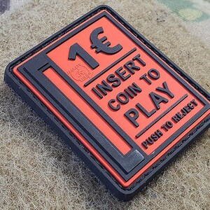 Könnte beinhalten: Schwarzer und orangefarbener Patch mit dem Text "1€ INSERT COIN TO PLAY PUSH TO REJECT".