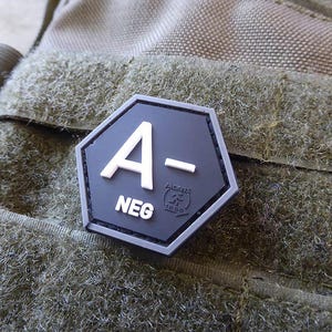 Könnte beinhalten: Ein schwarzer sechseckiger Patch mit weißem Text, der "A- NEG" lautet.