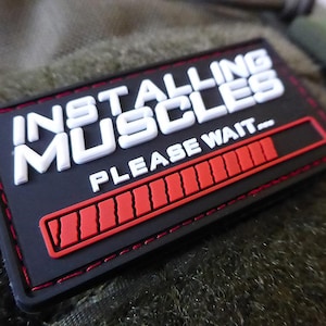 Op de afbeelding: Zwarte en rode patch met witte tekst die "Installing Muscles - Please Wait..." luidt, met een rode voortgangsbalk.