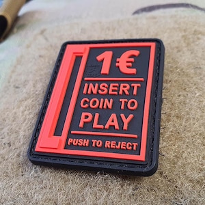 May include: Black and red rectangular patch with the text "1€ Insert Coin to Play Push to Reject".