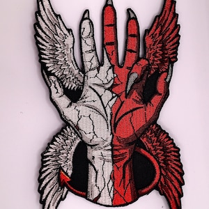 Op de afbeelding: Een geborduurde patch met een gespleten ontwerp van een hand. De linkerkant is wit met gebarsten huid en een gevederde vleugel, terwijl de rechterkant rood is met een klauwvormige vingertop, een gevederde vleugel en een gebogen staart aan de basis.