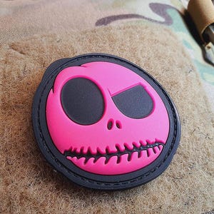 Può includere: Toppa ricamata rosa e nera con un design a forma di teschio. Il teschio ha una bocca cucita e due occhi neri.
