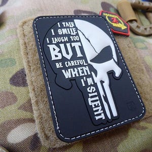 Könnte beinhalten: Schwarz-weißes Patch mit einem Totenkopf- und Knochen-Design. Der Text lautet "I talk I smile I laugh too BUT be careful WHEN I'M SILENT".