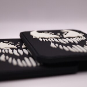 Peut inclure: Des patchs rectangulaires noirs avec un motif de cr&acirc;ne blanc stylis&eacute;. Les patchs sont empil&eacute;s, avec le motif repr&eacute;sentant des dents pointues et une partie sup&eacute;rieure incurv&eacute;e. Les patchs sont probablement faits d'un mat&eacute;riau durable.