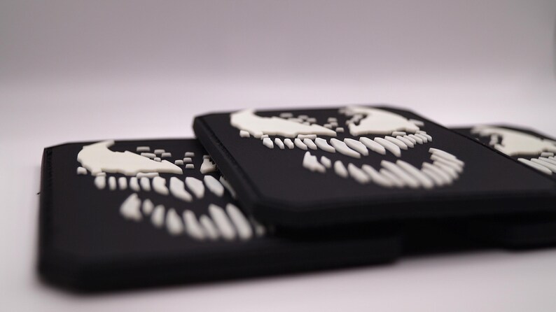 Peut inclure: Des patchs rectangulaires noirs avec un motif de cr&acirc;ne blanc stylis&eacute;. Les patchs sont empil&eacute;s, avec le motif repr&eacute;sentant des dents pointues et une partie sup&eacute;rieure incurv&eacute;e. Les patchs sont probablement faits d'un mat&eacute;riau durable.