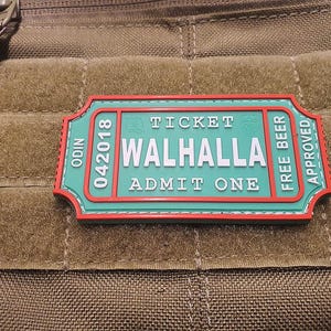 Può includere: Un biglietto verde e rosso con testo bianco che recita "Ticket Valhalla Admit One" e "Odin 042018 Free Beer Approved".