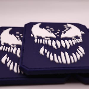 Op de afbeelding: Drie donkerblauwe patches met een wit, gestileerd monstergezicht. De patches zijn rechthoekig met afgeronde hoeken. Het monstergezicht heeft scherpe tanden en een dreigende uitdrukking, geschikt voor fans van strips en popcultuur.