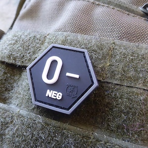 Könnte beinhalten: Ein schwarzer sechseckiger Patch mit weißem Text, der "O-" und "NEG" lautet.