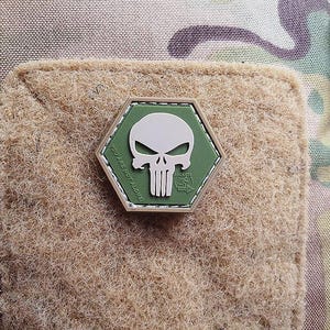 Könnte beinhalten: Ein sechseckiger Patch in Grün und Weiß mit einem weißen Totenkopf- und Knochenmotiv und dem Text "You are not alone".