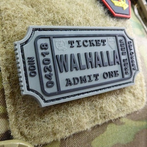 Może przedstawiać: Szary, przypominający bilet, naszywka z czarnym tekstem, który brzmi "Odin 042018 Ticket Valhalla Admit One Free Beer Approved".