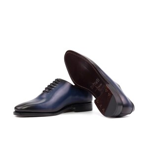 May include: A pair of blue leather lace-up dress shoes with a brown leather sole. The shoes are on a white background.