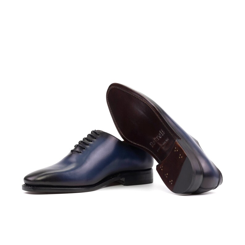 May include: A pair of blue leather lace-up dress shoes with a brown leather sole. The shoes are on a white background.