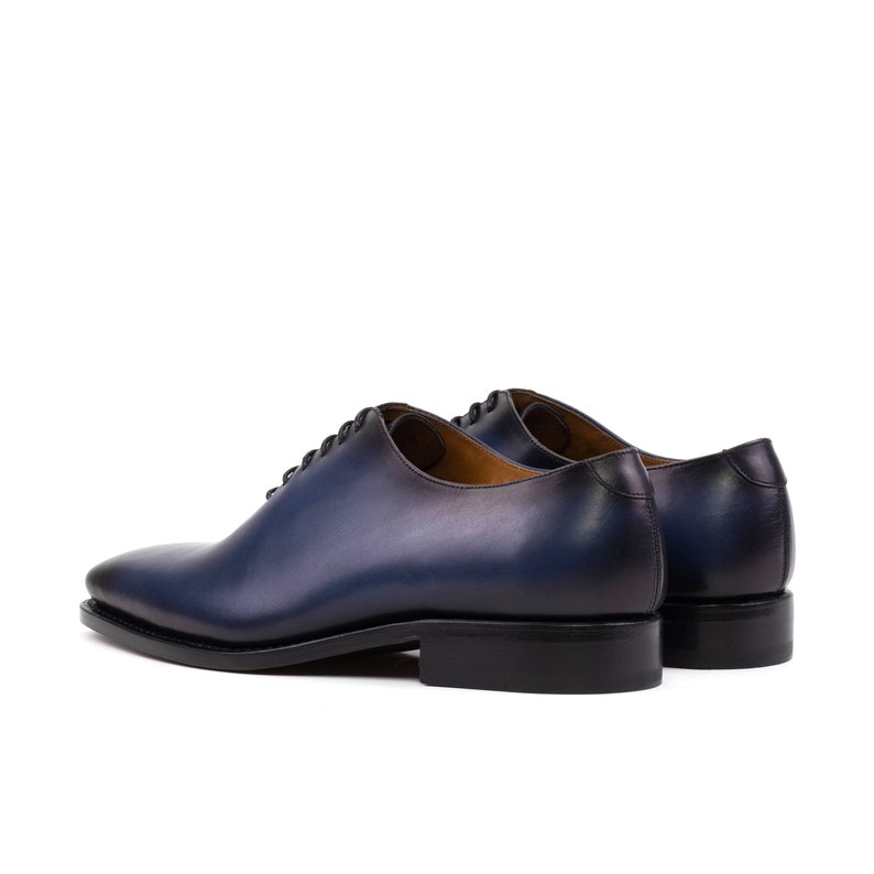 May include: A pair of blue leather lace-up dress shoes with a gradient effect. The shoes have a rounded toe and a low heel.