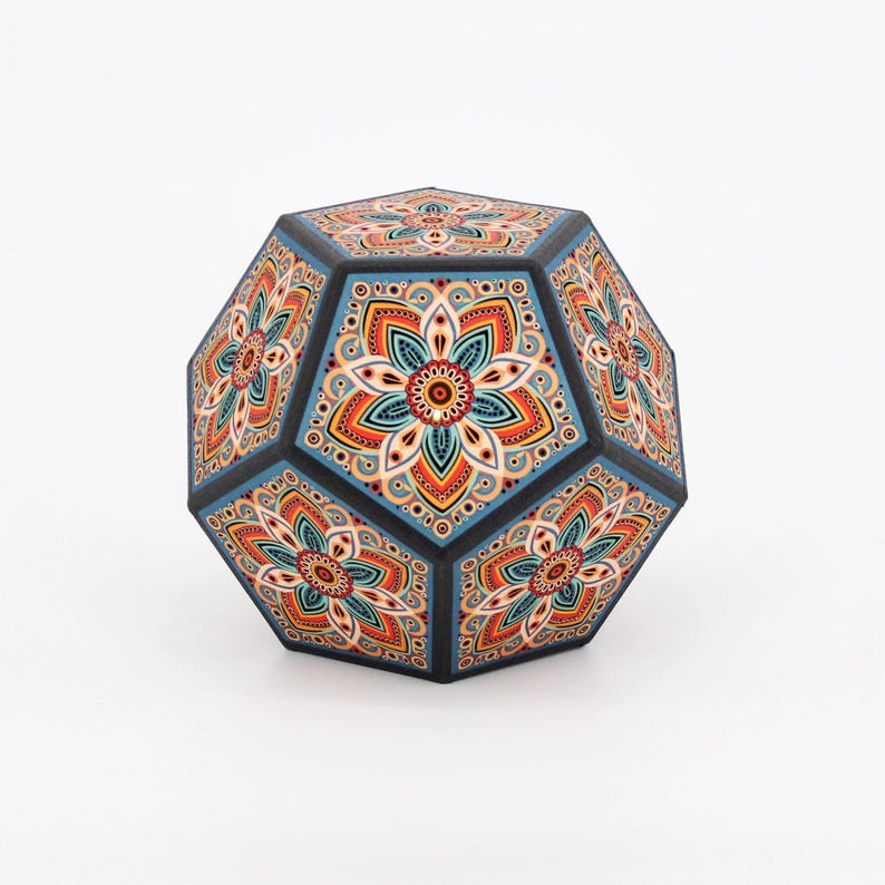 Pu&ograve; includere: Oggetto decorativo geometrico sfaccettato con motivo floreale. L'oggetto presenta una cornice nera con pannelli blu e un motivo ripetuto in arancione, rosso e verde acqua. L'oggetto &egrave; simmetrico e poggia su una superficie bianca.