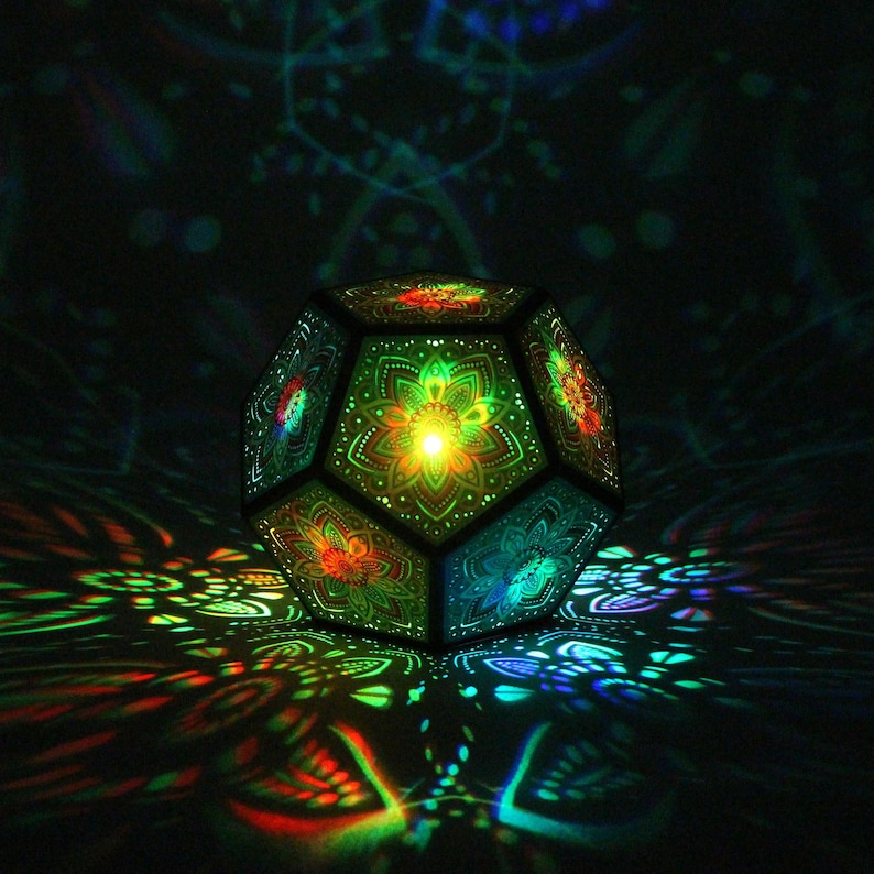 Pu&ograve; includere: Lampada geometrica sfaccettata con intricati motivi floreali. La lampada emette luce colorata, proiettando motivi vibranti sulla superficie circostante. Il design della lampada presenta tonalit&agrave; verdi, rosse e blu, creando un affascinante effetto visivo.
