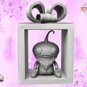 May include: A grey 3D printed figurine of a creature with a large head, large eyes, and a beard, sitting inside a white gift box with a grey bow on top. The box is on a pink background with floral designs.