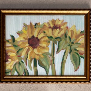 May include: A framed painting of three sunflowers with yellow petals and brown centers. The sunflowers are painted on a white background with light blue stripes.