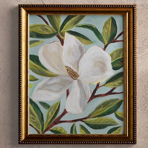 May include: A framed painting of a white magnolia flower with green leaves on a light blue background.