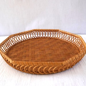 May include: A woven, octagonal basket tray in shades of brown. The tray features a woven base and a decorative, openwork border. The natural tones and texture suggest a rustic or bohemian style, suitable for serving or display.