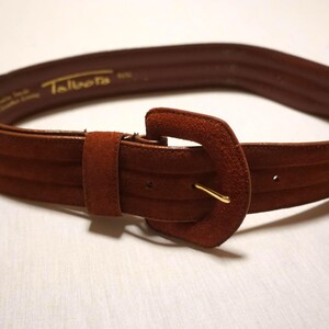 May include: A brown suede belt with a large, square buckle and a gold-colored metal pin. The belt has a textured design and the brand name "Talbots" is visible on the inside.
