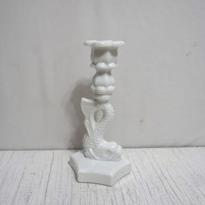 May include: White porcelain candlestick with a fish design and a flower-shaped candle holder.