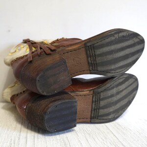 K&ouml;nnte beinhalten: Ein Paar braune Lederstiefeletten mit wei&szlig;en Ledereins&auml;tzen und Fransen. Die Stiefeletten haben eine schwarze Gummisohle mit einem Streifenmuster.