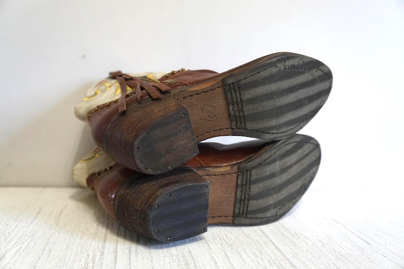 K&ouml;nnte beinhalten: Ein Paar braune Lederstiefeletten mit wei&szlig;en Ledereins&auml;tzen und Fransen. Die Stiefeletten haben eine schwarze Gummisohle mit einem Streifenmuster.
