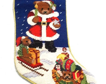 May include: A blue needlepoint Christmas stocking featuring a teddy bear dressed as Santa Claus, a smaller bear on a red sled, and a bear inside a green sack. The top cuff is dark blue with the gold embroidered text Let it Snow.