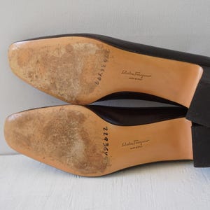 May include: A pair of brown leather heeled shoes with a brown leather sole. The shoes have a label on the sole that reads "Salvatore Ferragamo Made in Italy".
