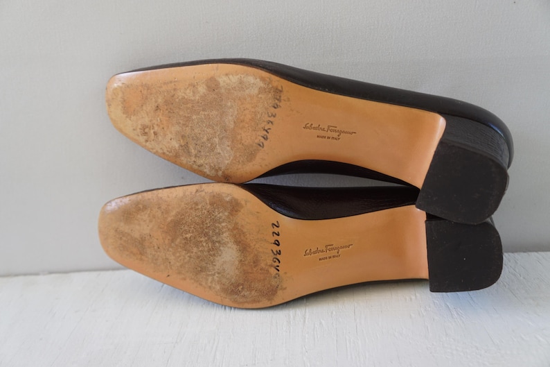 May include: A pair of brown leather heeled shoes with a brown leather sole. The shoes have a label on the sole that reads "Salvatore Ferragamo Made in Italy".
