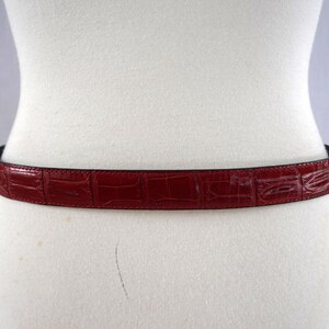 K&ouml;nnte beinhalten: Ein weinroter G&uuml;rtel mit Krokodilleder-Textur ist um eine Schaufensterpuppe gelegt. Der G&uuml;rtel ist schmal, mit einer dunklen Unterseite. Ein klassisches Accessoire.