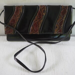 May include: A rectangular black shoulder bag featuring a glossy finish and two diagonal panels with a brown and black snakeskin-like texture. The bag includes a thin black shoulder strap and a flap closure that covers the main compartment.