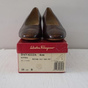 May include: A pair of brown leather women's shoes with a crocodile print. The shoes are in a box with the brand name Salvatore Ferragamo and the model name Davallia. The box also includes the size 10 1/2 B and the heel height, 4 cm.