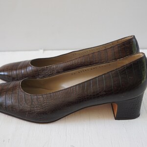 May include: A pair of brown leather heeled pumps with a crocodile embossed pattern.